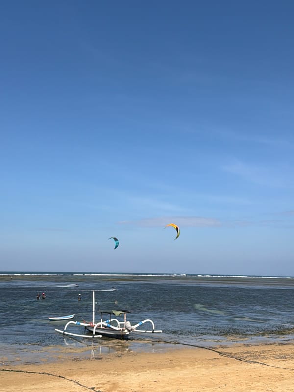 Busy morning on a Denpasar beach: kites, boats, and beachside strollers