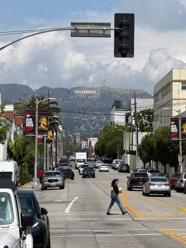 Pedestrian walks LA street beneath iconic Hollywood sign