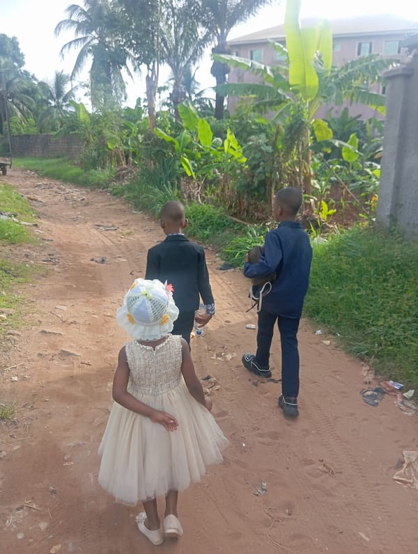 Children walk dirt path amid vegetation in Nkpor, Nigeria