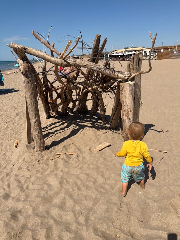Toddler explores a sunny Sérignan beach near driftwood