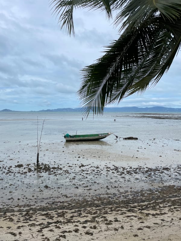 Green boat rests on low-tide beach in Thailand