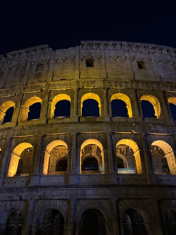 Rome's Colosseum glowing after dark, crowds outside