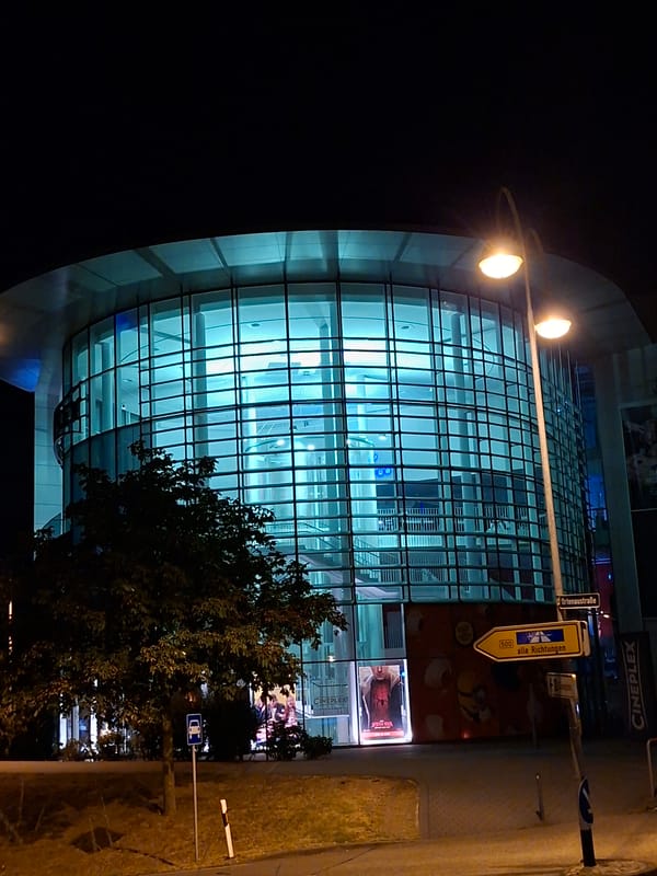 Cineplex exterior glows at night with colorful illuminated facade