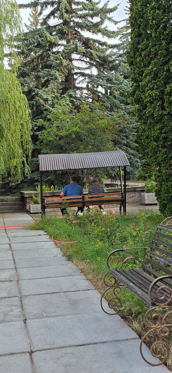 Weathered public sculptures and a shaded bench in rural Kyrgyzstan