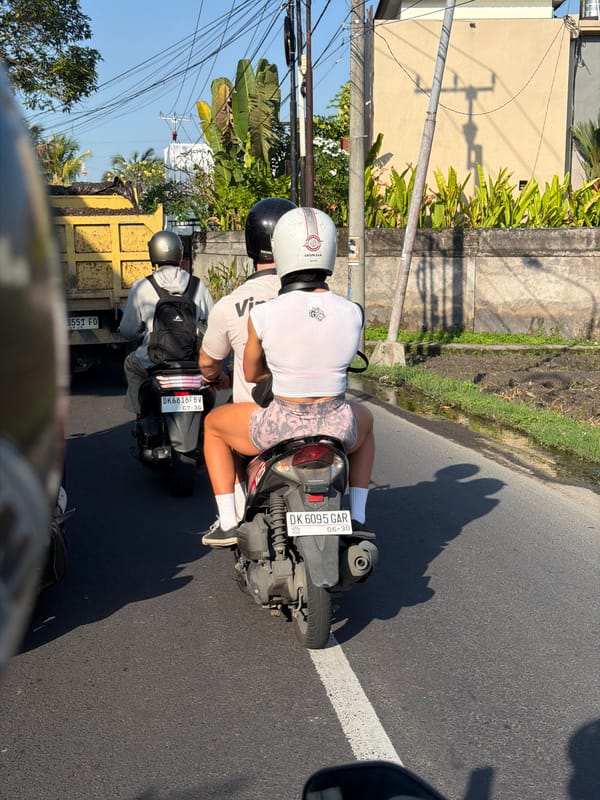 Motorcyclists cruising a tree-lined road in Mengwi, Bali