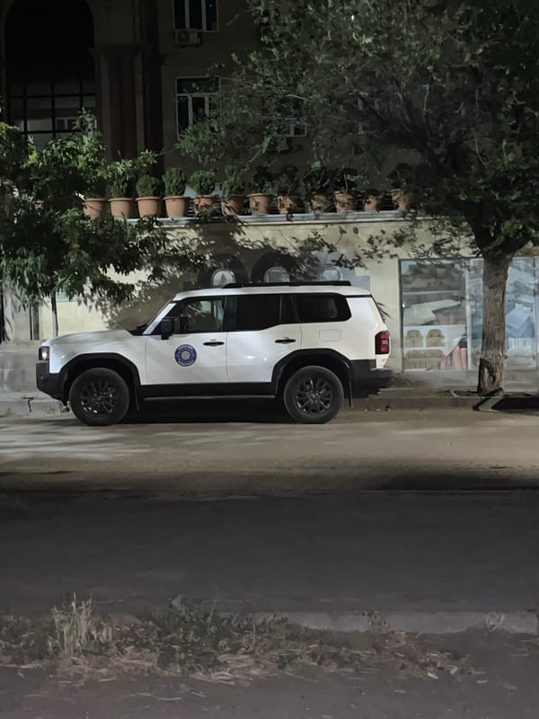 White SUV parked at night outside a building with potted plants