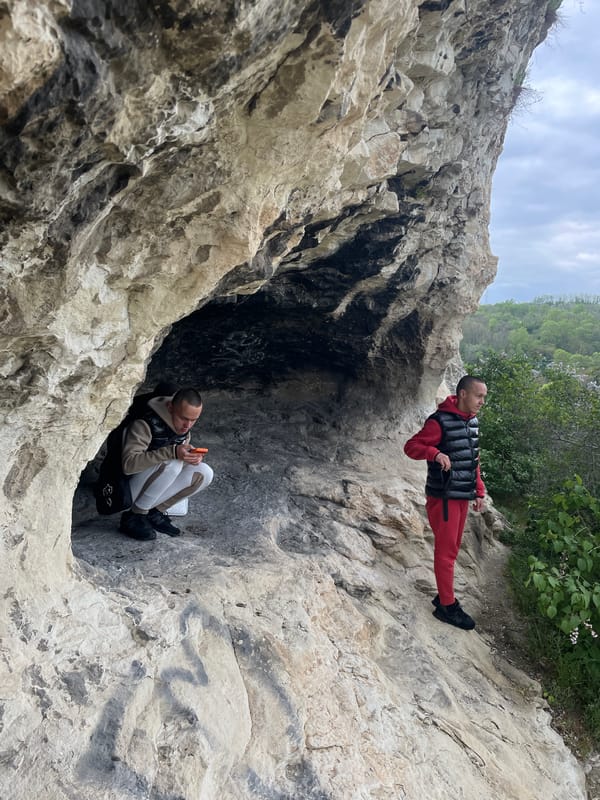 Three people explore rocky hillside cave area