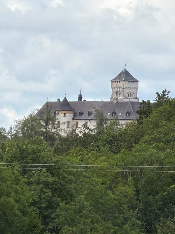 Hilltop castle peeks through summer trees in northern Bavaria