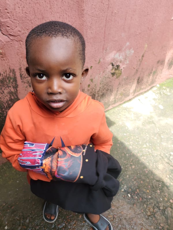 Kid in a Batman hoodie chills with a dog in Jos