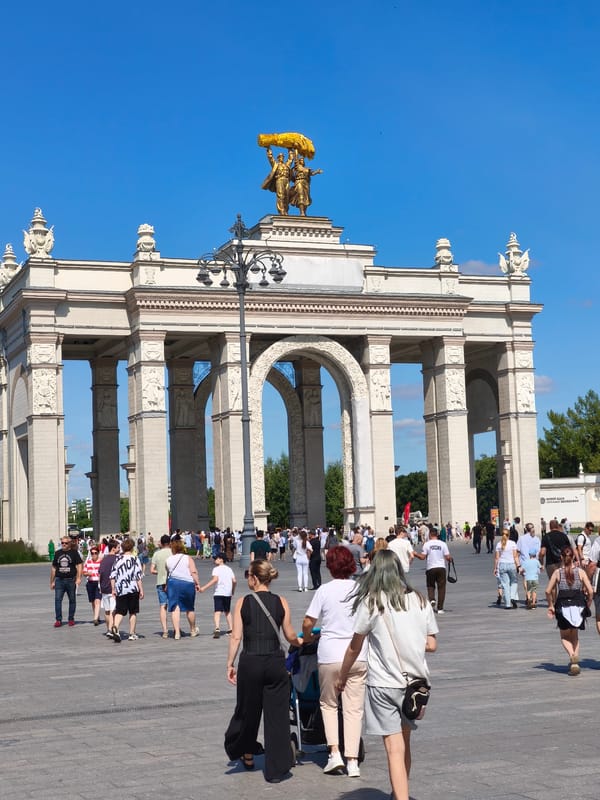 Crowds fill a grand plaza beneath golden wheat sculpture