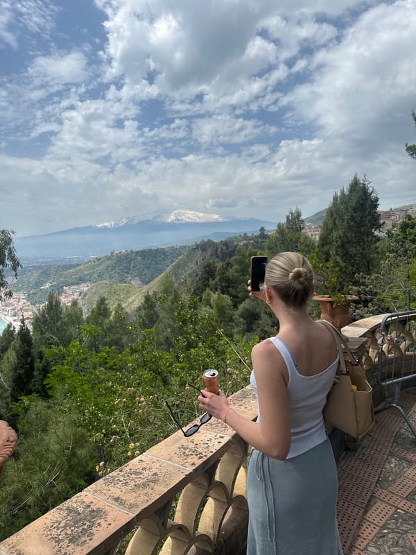 Woman enjoys scenic Taormina balcony view with mobile device