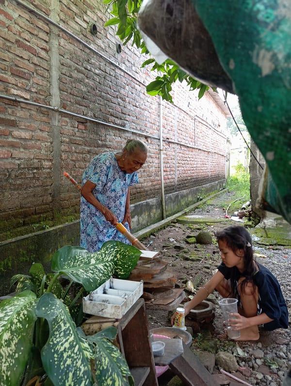 Elderly woman sweeps yard with child, cat in Baron