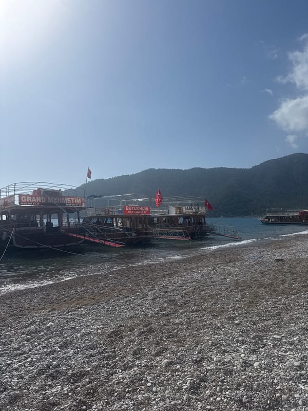 Tour boats dock at Kumluca beach as morning visitors gather