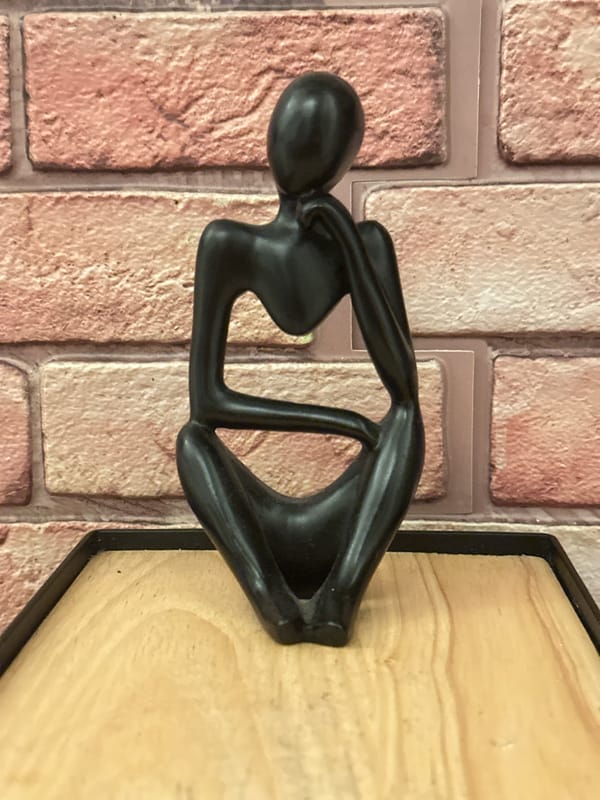 Black contemplative sculpture observed on London brick wall display