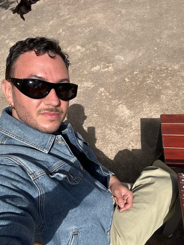 Person in sunglasses and denim jacket sits by bench in Madrid