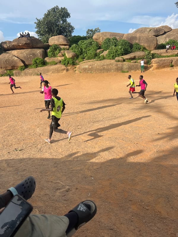 Pickup football on a dusty Jos field beneath granite outcrops