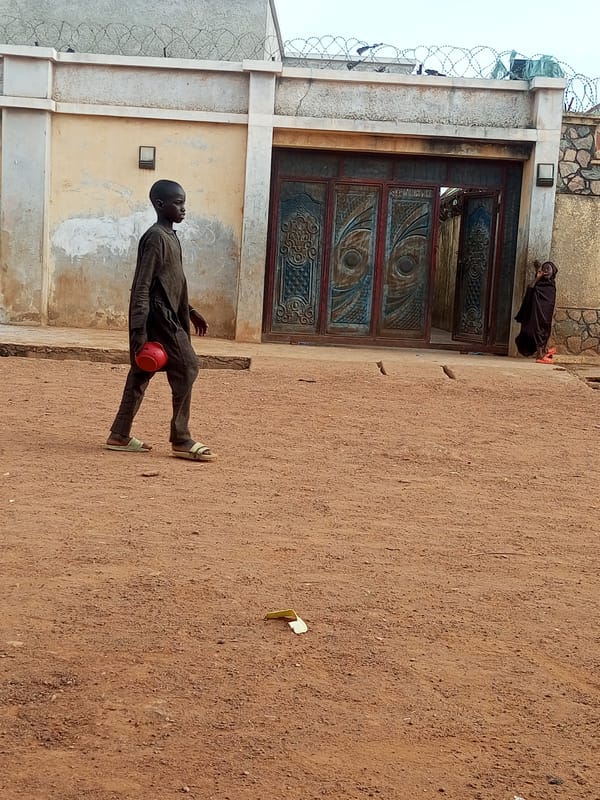 Boy carries red container across dusty yard in Nigeria