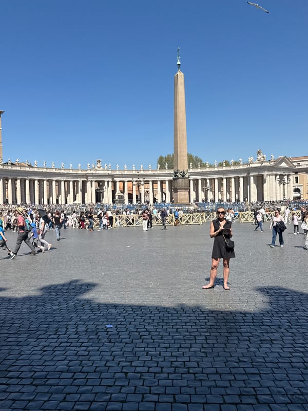 Crowd gathers at St. Peter's Square with umbrellas, large screen