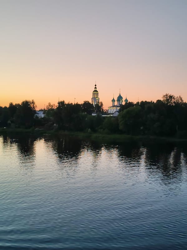 Dusk settles over a river with a church on the far bank.