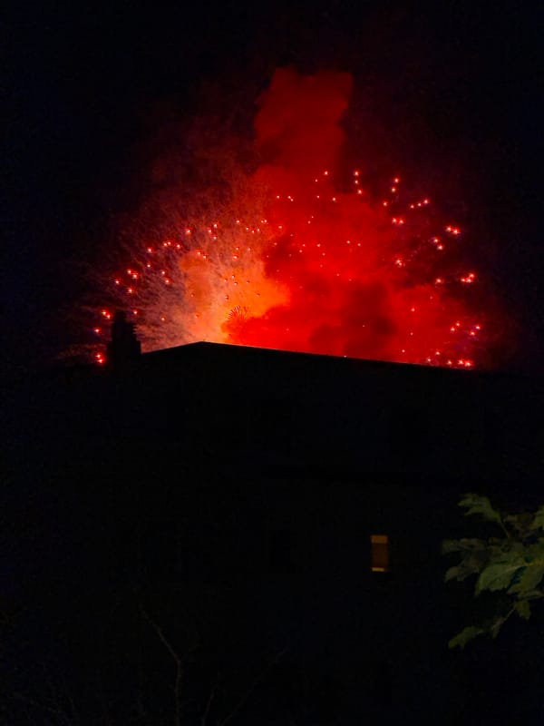 Nighttime fireworks burst over a residential building in colorful display