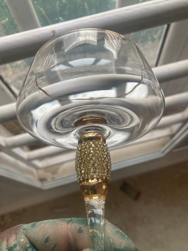 Paint-splattered hand holds wine glass during renovation work in Jos