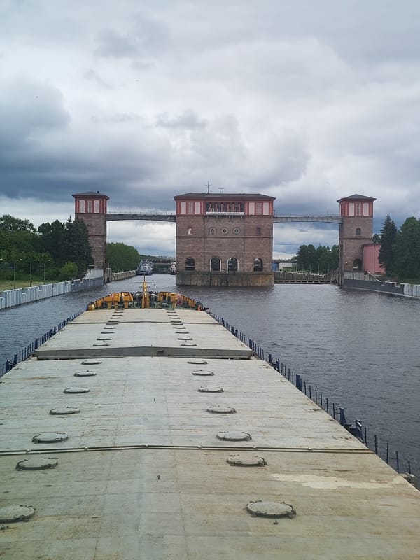 Barge transits Rybinsk Lock with tugboat assistance under overcast skies