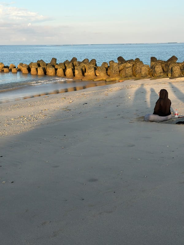 Woman in hijab sits by breakwater at Kuta Beach