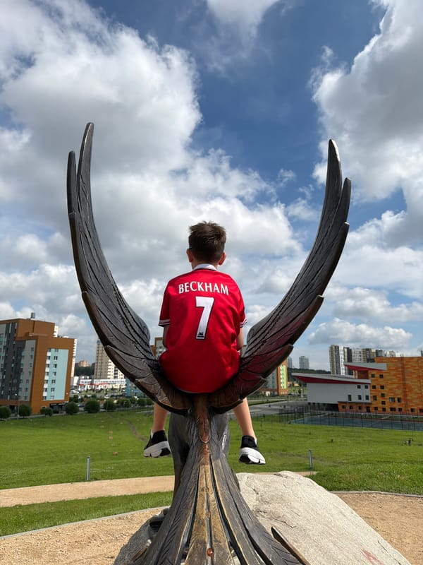 Climbing a bronze phoenix sculpture in Yekaterinburg, Beckham jersey on