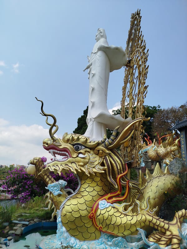 Visitor documents Vietnamese temple complex with Buddhist statues and gardens
