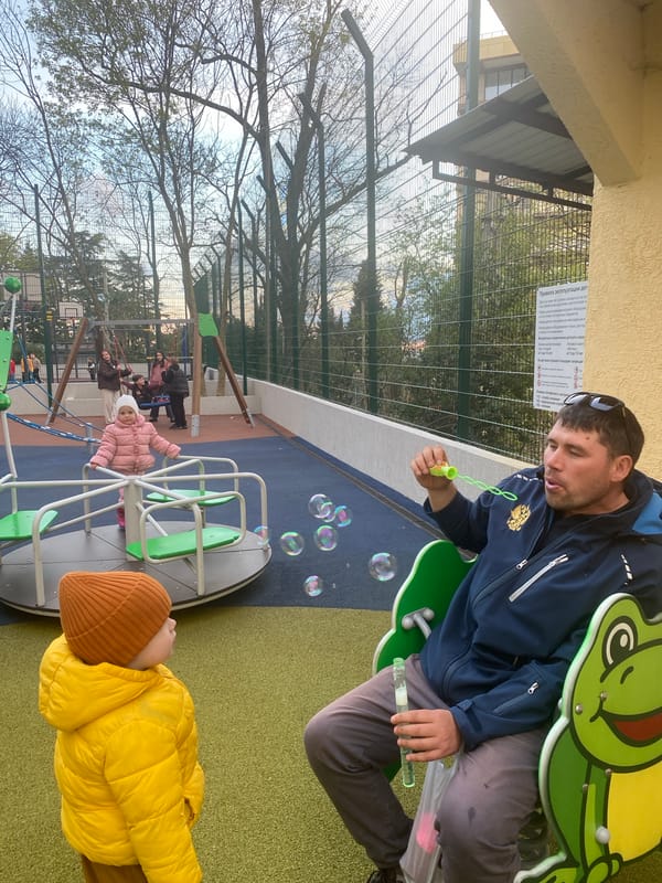 Man blows bubbles for child at Sochi playground