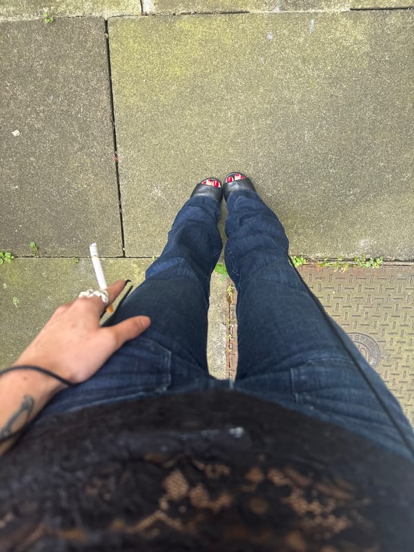 Person stands on cracked London sidewalk with sprouting vegetation