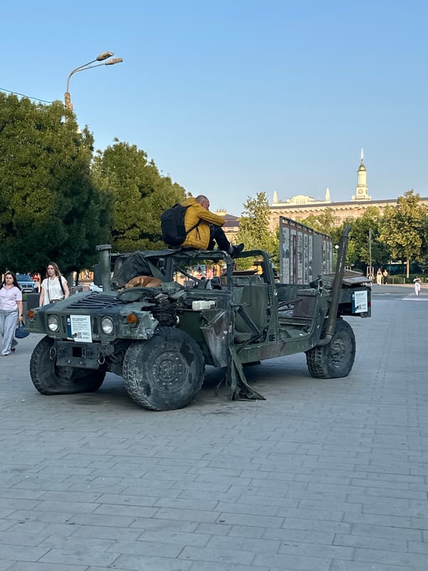 Kyiv street life alongside a displayed war vehicle, summer afternoon