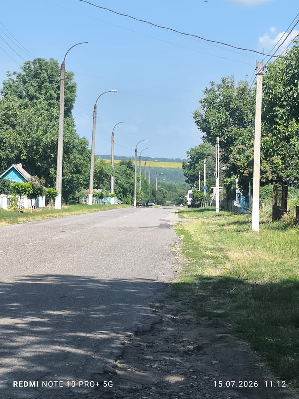 Cracked rural road winds through green, hilly terrain