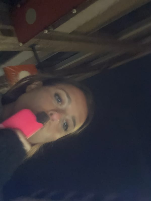 Person photographed vaping pink e-cigarette near metal wall at night