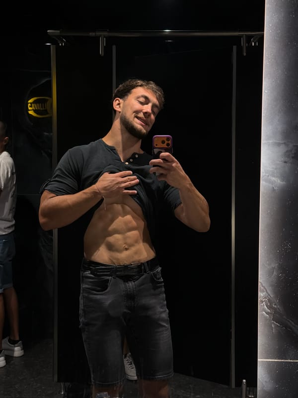 Mirror selfie in a Kiten restroom, low light, casual fit.
