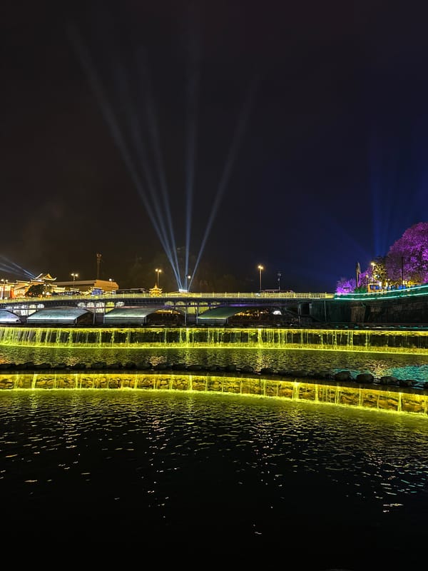 Colorful nighttime illumination display features waterfall and bridge lighting