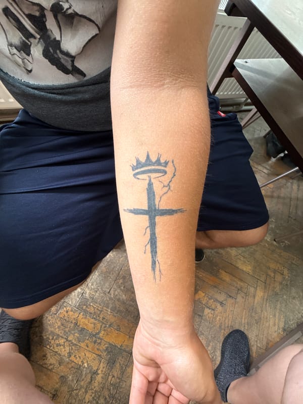 Young man with tattoo writes, uses phone at desk