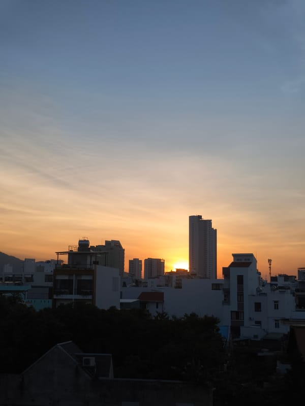 City skyline glows at sunset, sun dipping behind buildings