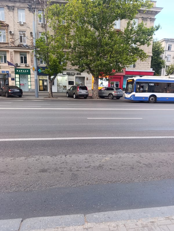 City bus rolls through an urban street past a classical building