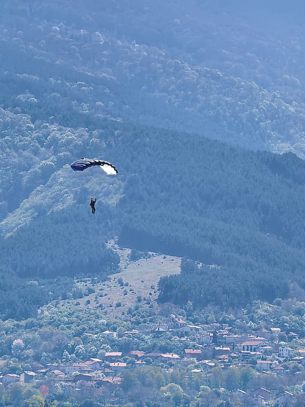 Skydivers with colorful parachutes descend over Bulgarian mountain village