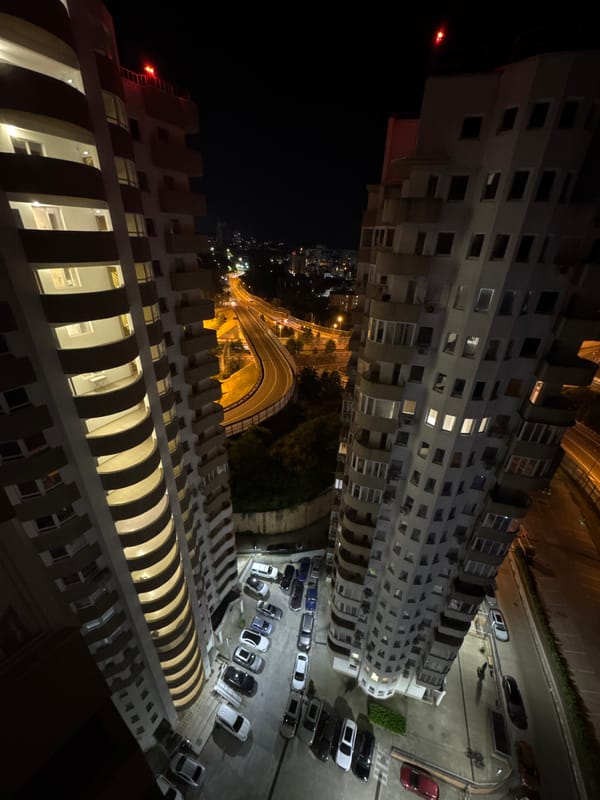 Woman at window observes Sochi nighttime cityscape from apartment