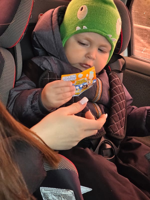 Baby in cartoon hat holds packet during car ride