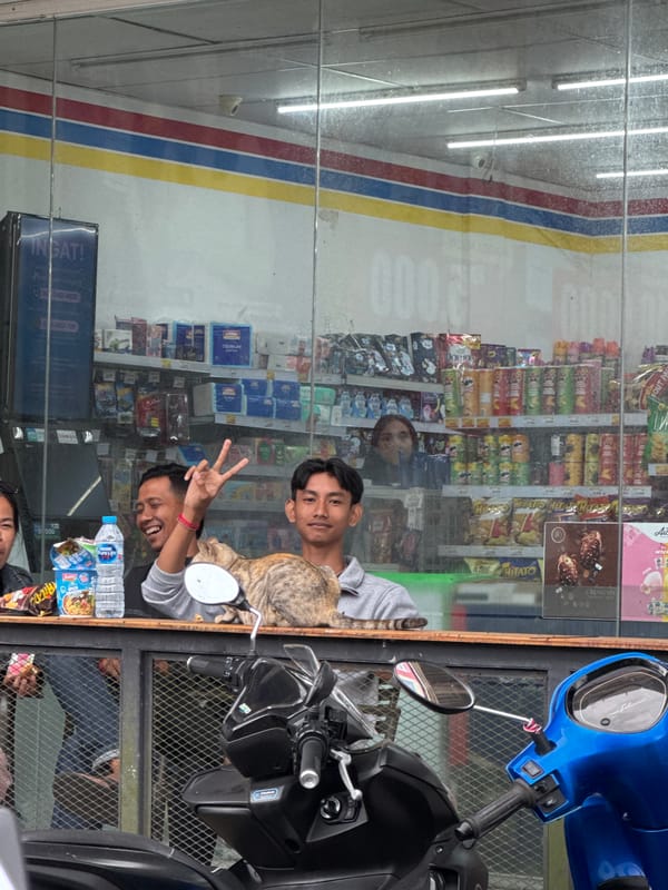 Two men pose outside Kintamani storefront with motorcycle, cat