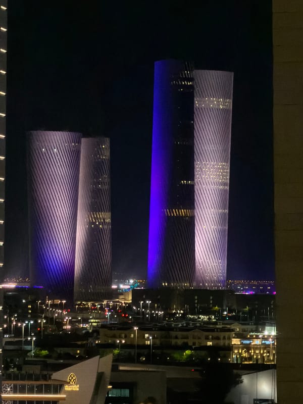 Illuminated ribbed towers glow over a city waterfront at night