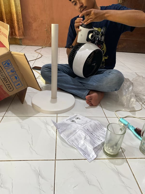 Man assembles fan, rests on floor in Madiun home