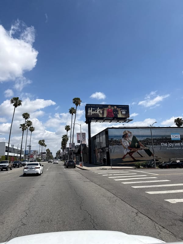 Palm-lined LA street scene with billboards and traffic