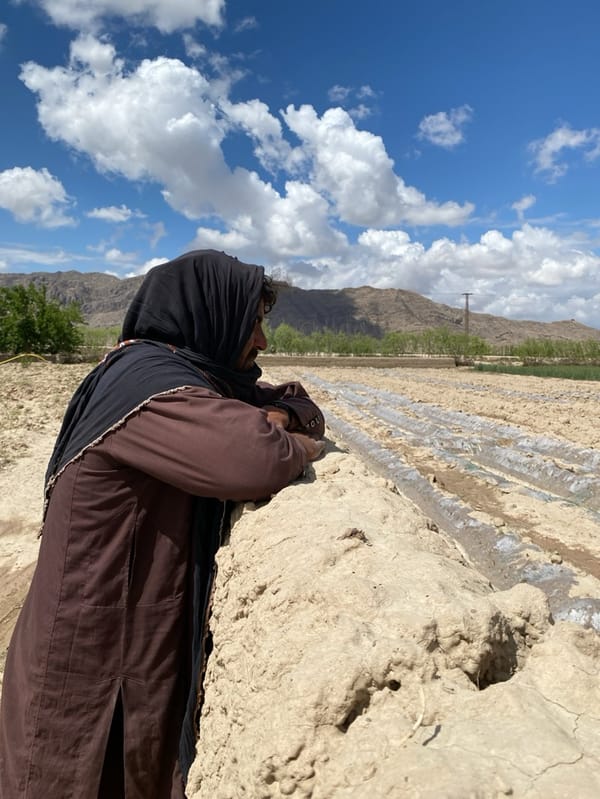 Man in traditional dress observed by mud wall in rural Afghanistan