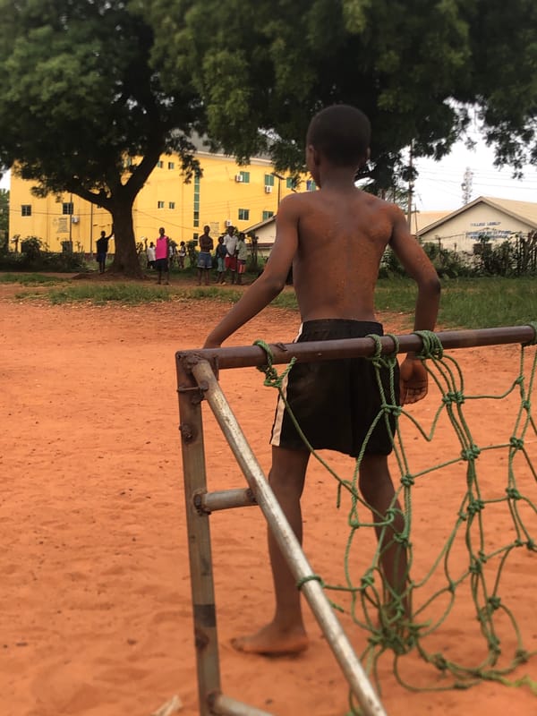 Young men play informal soccer on dirt field in Nigeria
