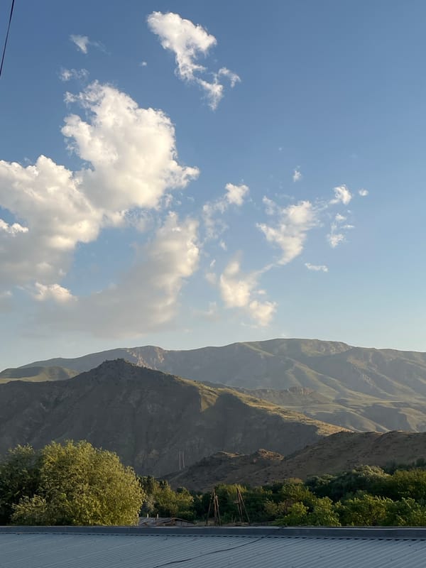 Meat on skewers grilling outdoors beneath mountain skies