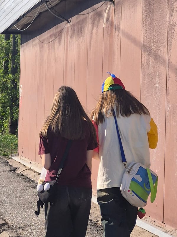 Two people stand by plank wall near greenery